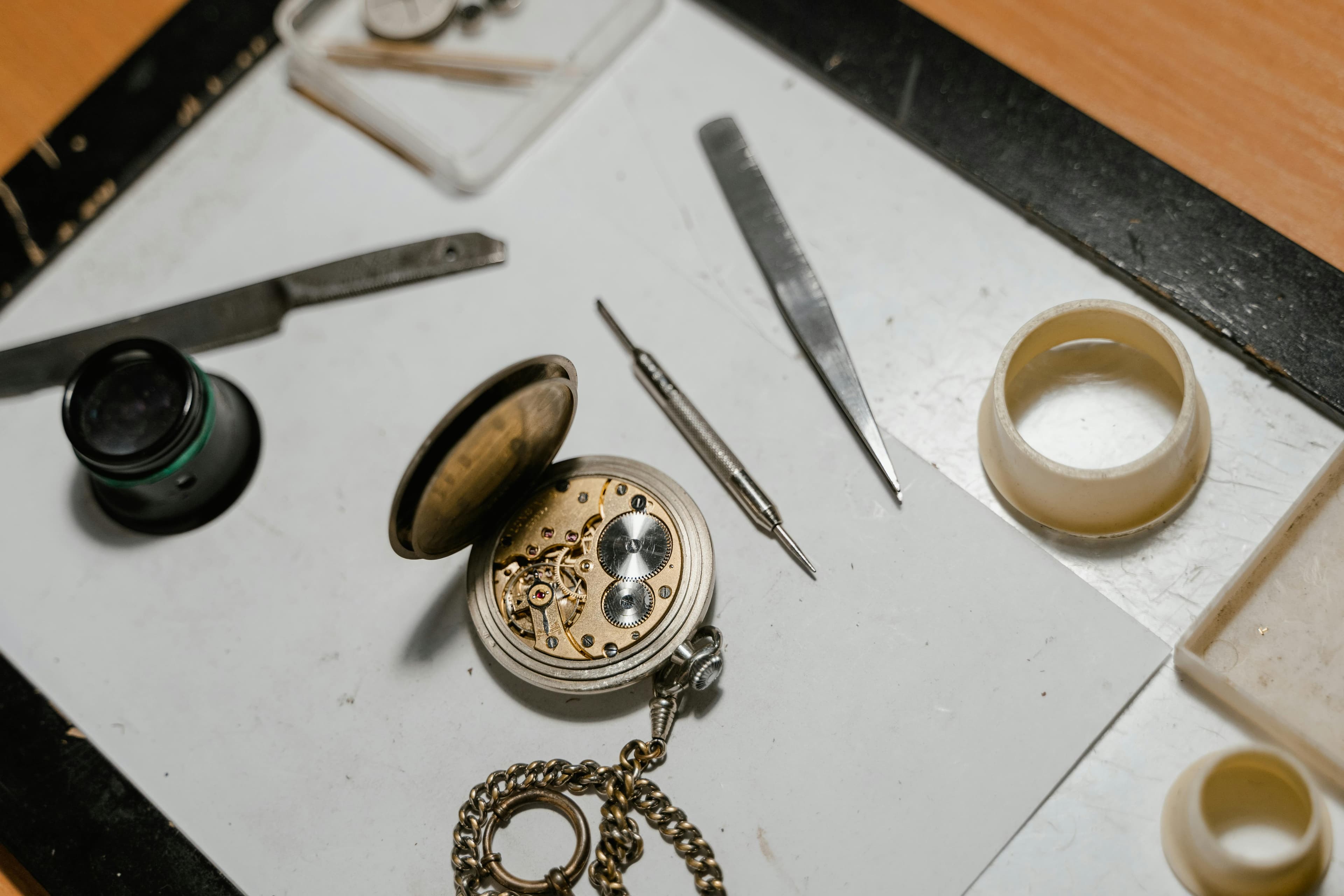 Open pocket watch with loupe, tweezers, and movement holder on a watchmaker's bench